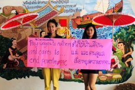 Two Southeast Asian women hold a banner in English and Thai